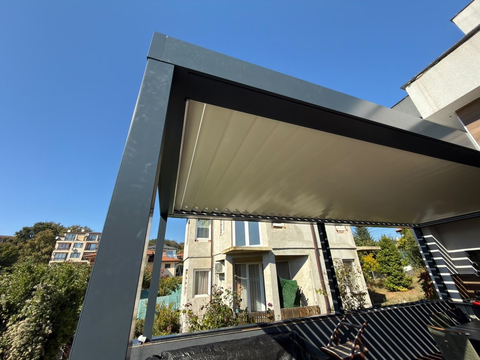 Dark pergola frame and closed light-coloured roof louvres above a residential terrace.